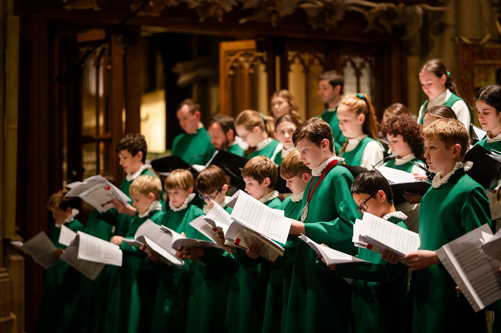 A mixed group of choristers in green robes, holding sheet music in a church