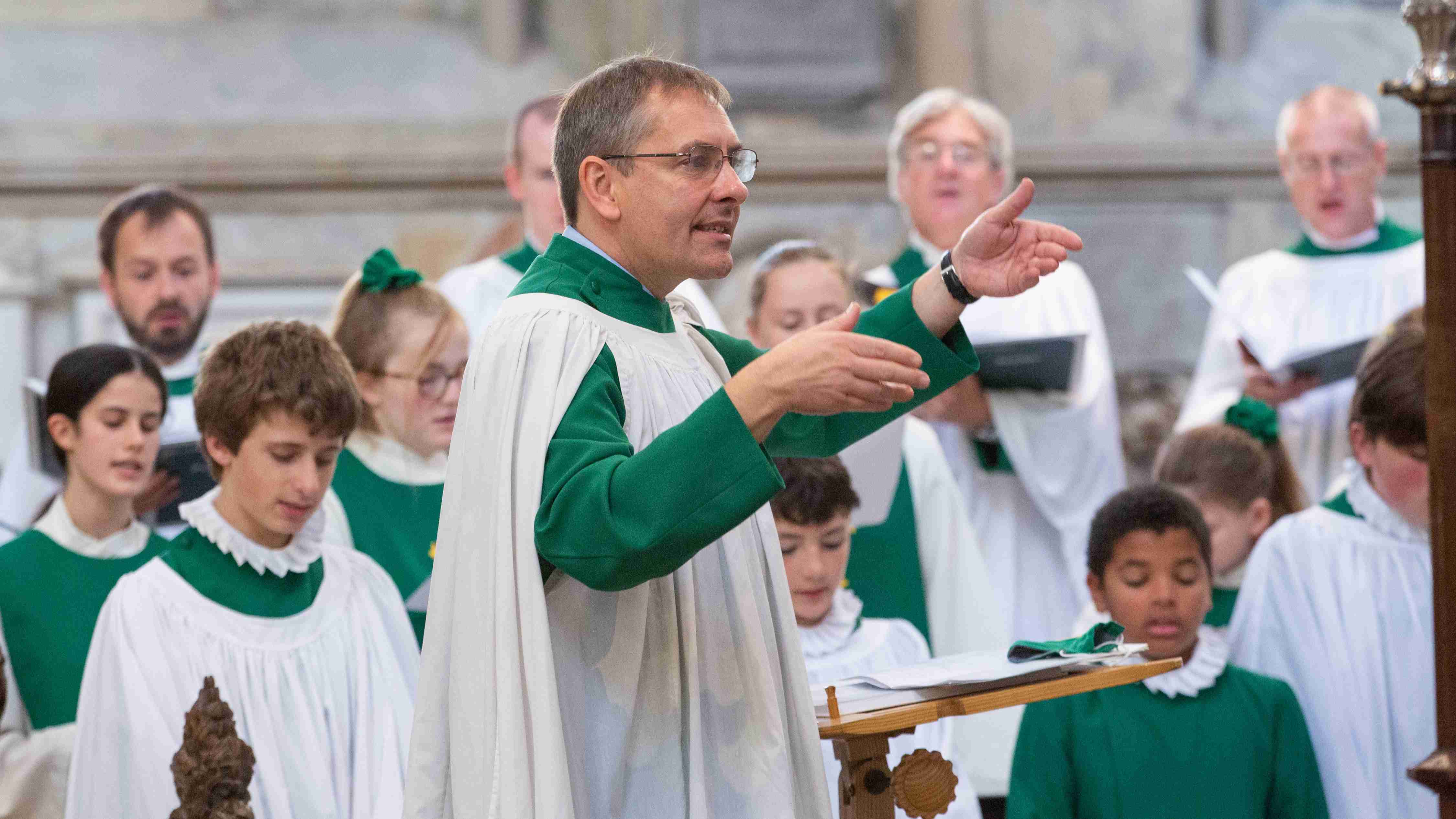 Conductor in green and white robes conducting a choir in similar robes